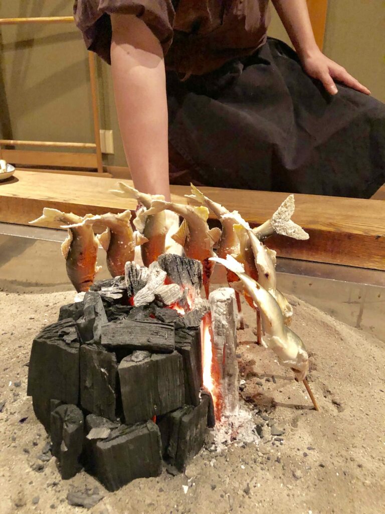 Charcoal-grilled ayu river fish prepared at the famous Yanagiya Restaurant in Gifu, Japan—each skewered and cooked slowly over an open irori hearth, representing one of Japan’s most traditional and revered styles of countryside cuisine.