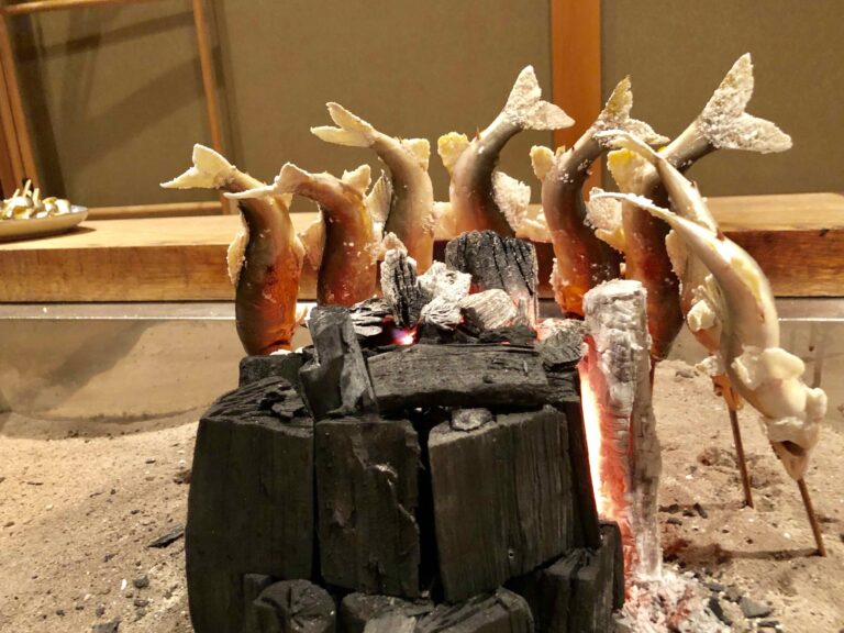 Skewered ayu sweetfish slow-grilled over charcoal on an irori hearth at Yanagiya in Gifu, Japan’s legendary wild meat and river fish cuisine restaurant known for seasonal game meat and river fish.