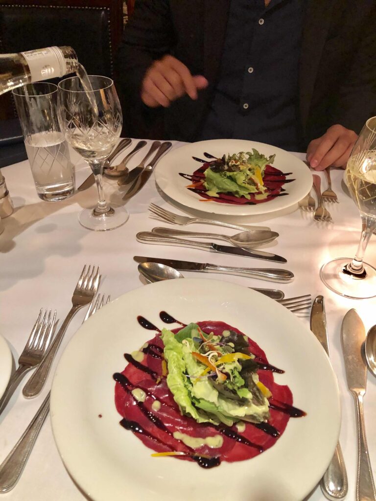 A beautifully plated smoked salmon appetizer served in the elegant dining car of The Blue Train, set on a white tablecloth with polished silverware and crystal glasses, capturing the refined fine-dining experience aboard South Africa’s iconic luxury train.
