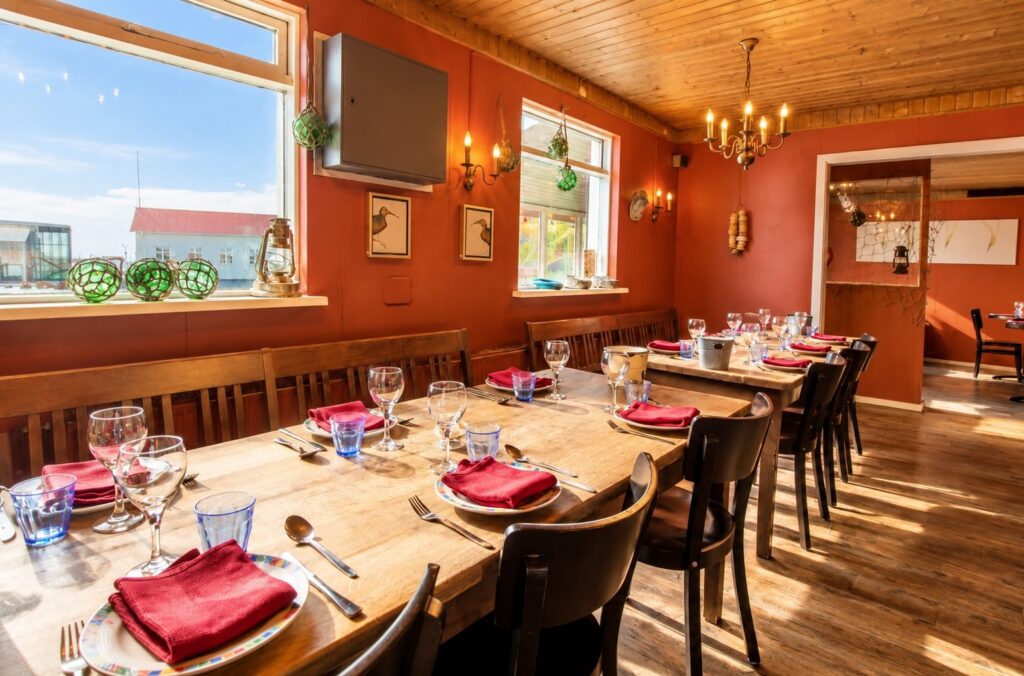 Warmly lit rustic dining room inspired by Fjöruborðið lobster restaurant in Stokkseyri, Iceland, with wooden tables, red napkins and blue drinking glasses.