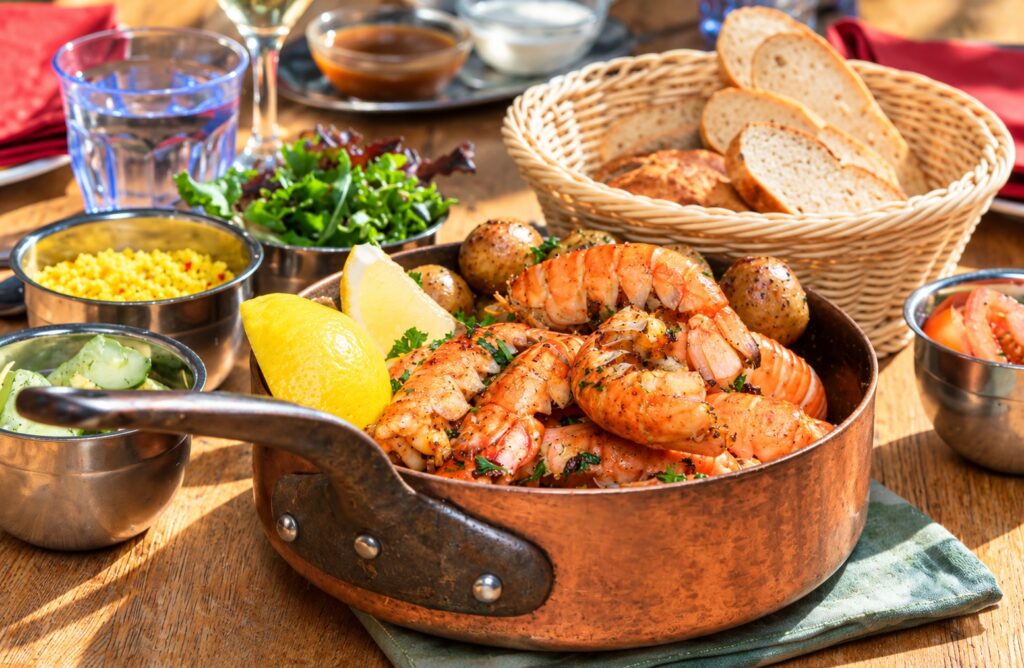 Icelandic langoustines in a copper pan with lemon, potatoes and bread, illustrating the famous lobster meal at Fjöruborðið in Stokkseyri, Iceland.