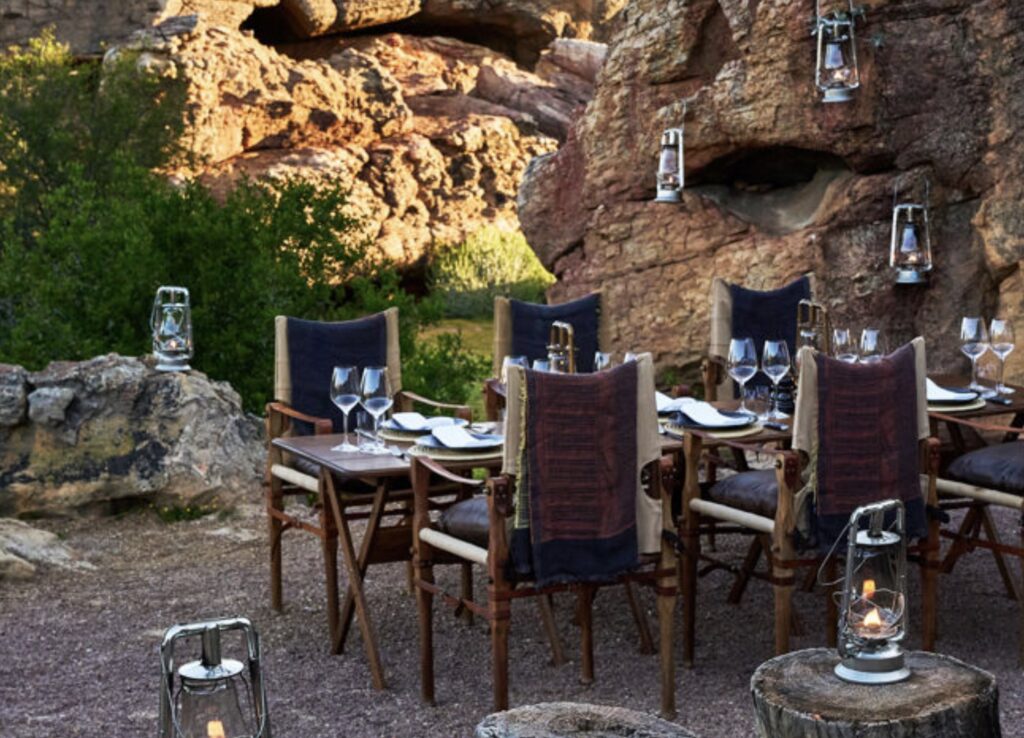 Outdoor dining setup for a champagne breakfast among ancient rock formations at Bushman’s Kloof in South Africa’s Cederberg Mountains. Elegant tables, lanterns, and white linens create a luxurious wilderness experience surrounded by nature and sandstone cliffs.