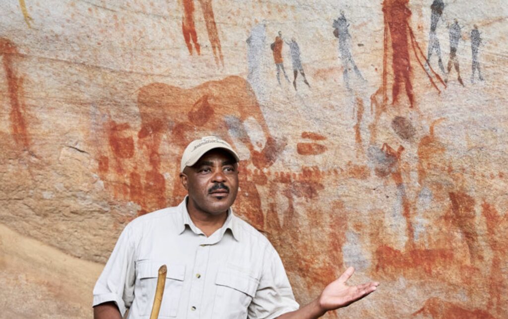 Local guide at Bushman’s Kloof explaining ancient San rock art painted on cave walls in the Cederberg Mountains of South Africa. The ochre and red figures, some over 10,000 years old, reveal the deep spiritual and cultural heritage of the San people.