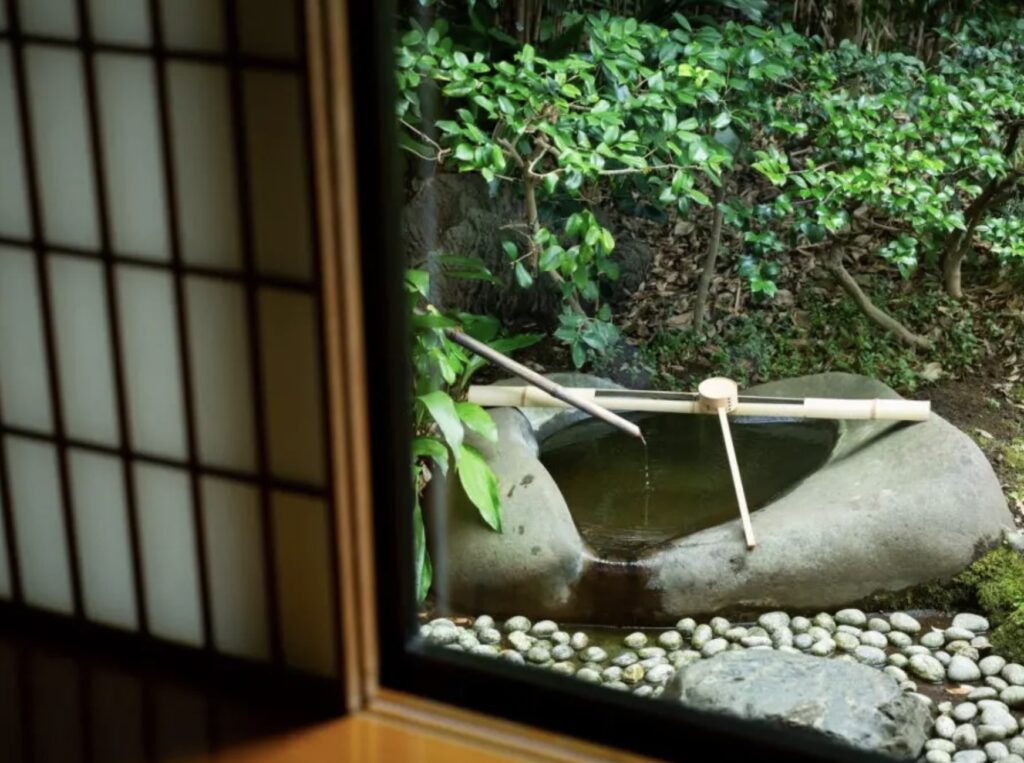 View from inside a traditional Japanese tea house at Hotel Chinzanso Tokyo looking onto a stone water basin and moss garden, framed by shoji screens, used for Omotesenke tea ceremonies