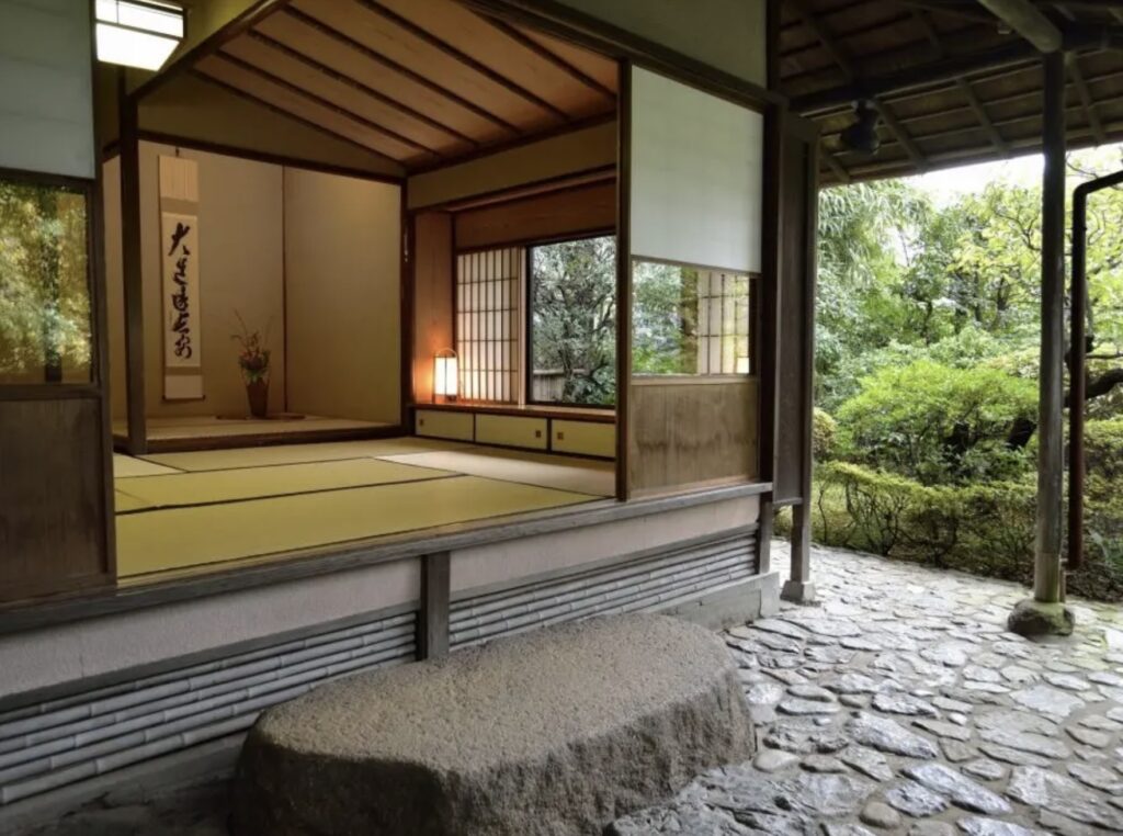 Interior of a historic Japanese tea house at Hotel Chinzanso Tokyo featuring tatami mats, sliding shoji doors, a hanging calligraphy scroll, and a stone garden path used for traditional Omotesenke tea ceremonies