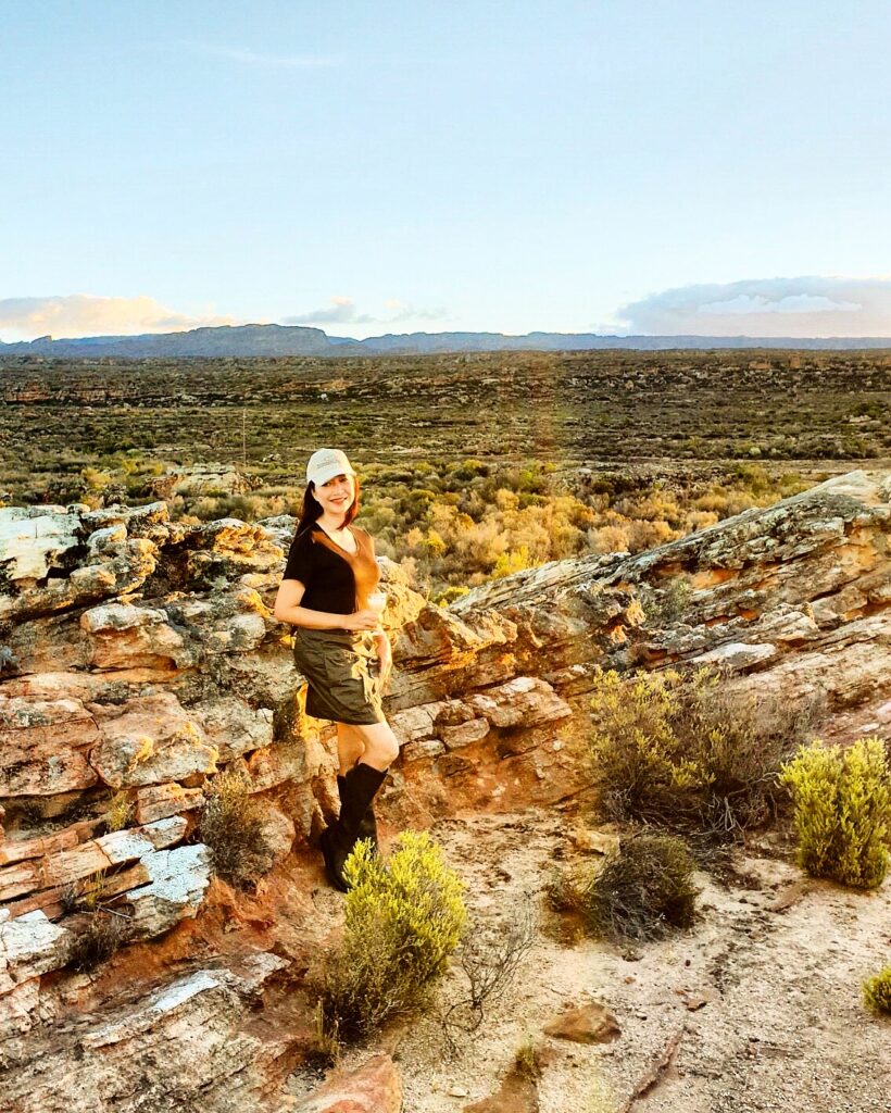 Traveler standing on sunlit rocks in the Cederberg Mountains at Bushman’s Kloof, surrounded by rugged sandstone terrain and golden light. The scene reflects the quiet beauty and wild freedom of South Africa’s highland wilderness.