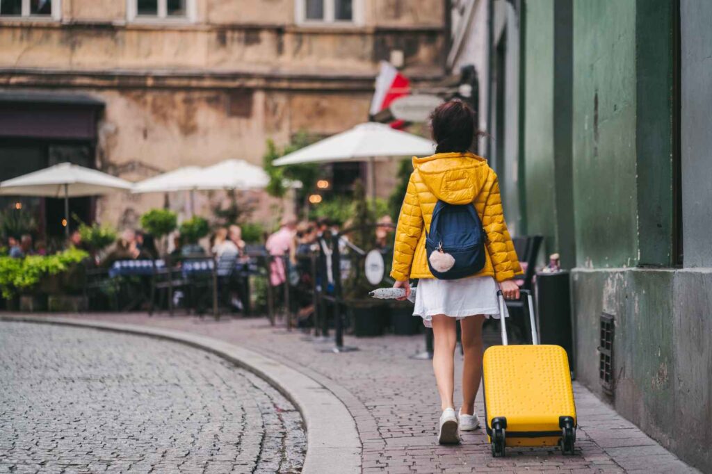 Solo female traveler in yellow jacket walking along a cobblestone street with a bright yellow suitcase, symbolizing safe, confident, and independent women’s travel — emphasizing awareness, connectivity, and smart solo journey planning.