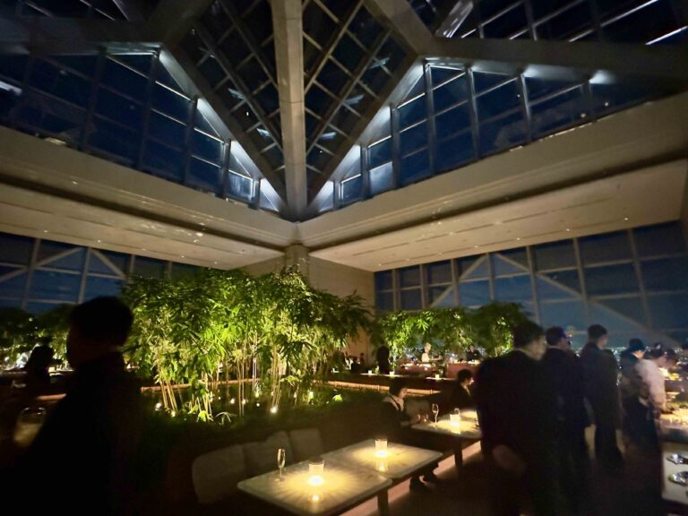 Guests gather beneath the glass atrium during the Park Hyatt Tokyo reopening party, surrounded by candlelit tables and a freshly replanted bamboo garden that symbolizes renewal and quiet luxury above the Shinjuku skyline.