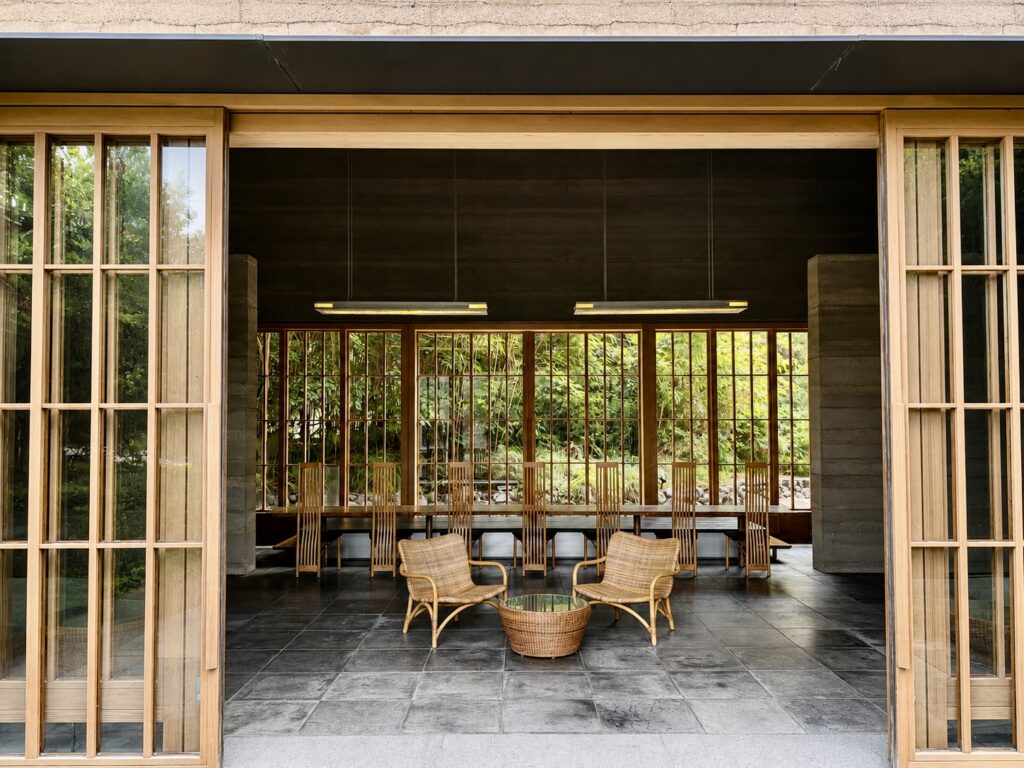 Open-air lobby at Numazu Club designed by architect Akira Watanabe, with timber sliding doors, woven chairs and garden views in Numazu, Shizuoka, Japan.