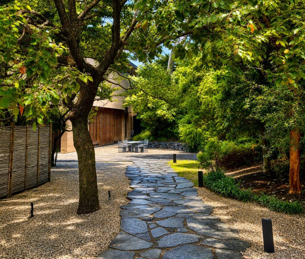 Stone pathway through the gardens of Numazu Club in Shizuoka, Japan, leading to the Michelin One-Key luxury ryokan surrounded by mature trees and traditional Japanese landscaping. Photographed by Travelife Magazine.