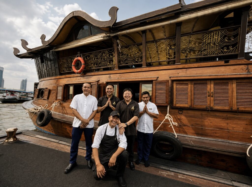 Anantara boat crew beside Loy Dream, Anantara’s restored Thai rice barge, during a private Bangkok river cruise