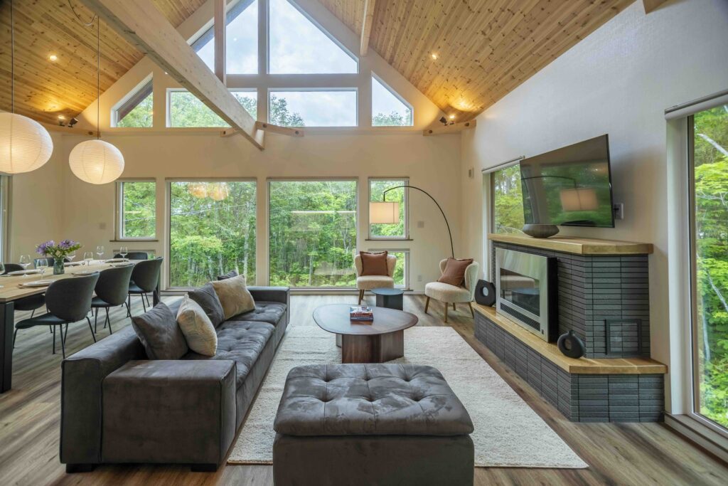 Open-plan living room at Soga Forest Chalet in Niseko, Hokkaido, featuring vaulted timber ceilings, a fireplace and floor-to-ceiling forest views.