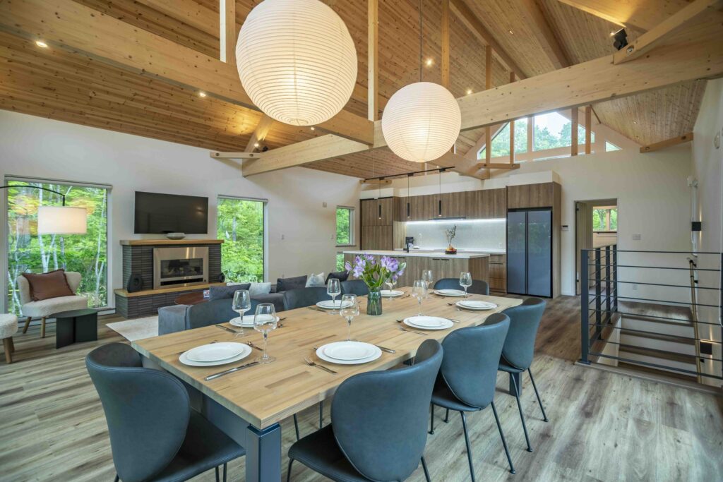 Open-plan dining and living room at Elite Havens Soga Forest Chalet in Niseko, Japan, with timber ceilings, pendant lights and forest views.