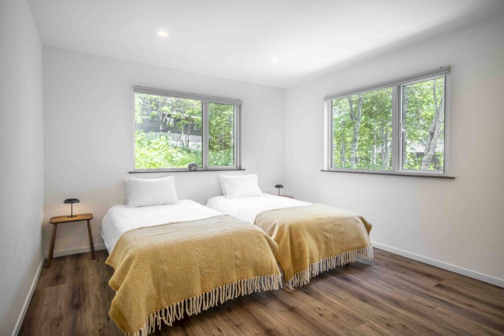Twin bedroom with two single beds, wooden flooring and forest-view windows at Elite Havens Soga Forest Chalet in Niseko, Hokkaido, Japan.