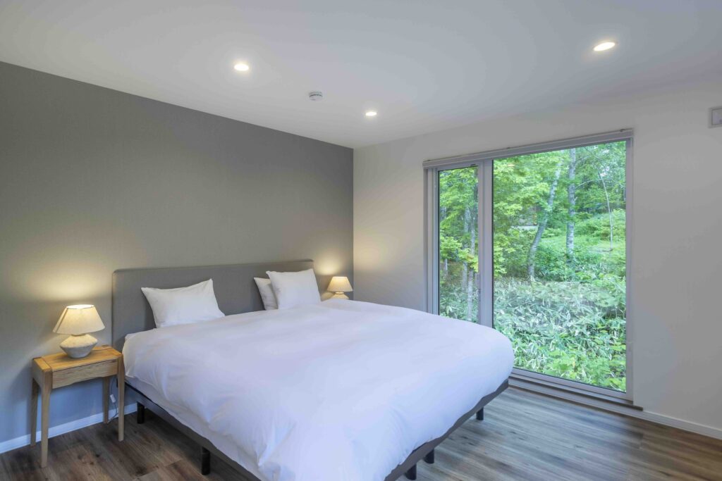 Serene bedroom with a queen-size bed, soft white linens and a forest-view window at Soga Forest Chalet in Niseko, Hokkaido, Japan.