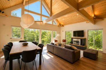 Open-plan living and dining room at Soga Forest Chalet in Niseko, Hokkaido, with vaulted timber ceilings, exposed beams and floor-to-ceiling forest views.