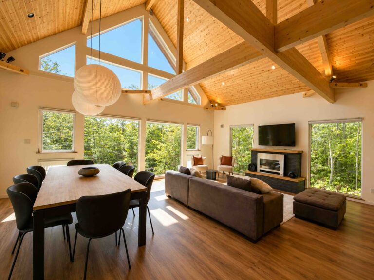 Open-plan living and dining room at Soga Forest Chalet in Niseko, Hokkaido, with vaulted timber ceilings, exposed beams and floor-to-ceiling forest views.
