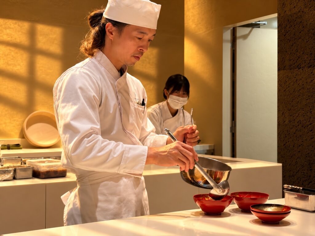 Japanese chef in a white uniform preparing dishes in an open kitchen at Pasona Natureverse Retreat on Awaji Island, Japan.