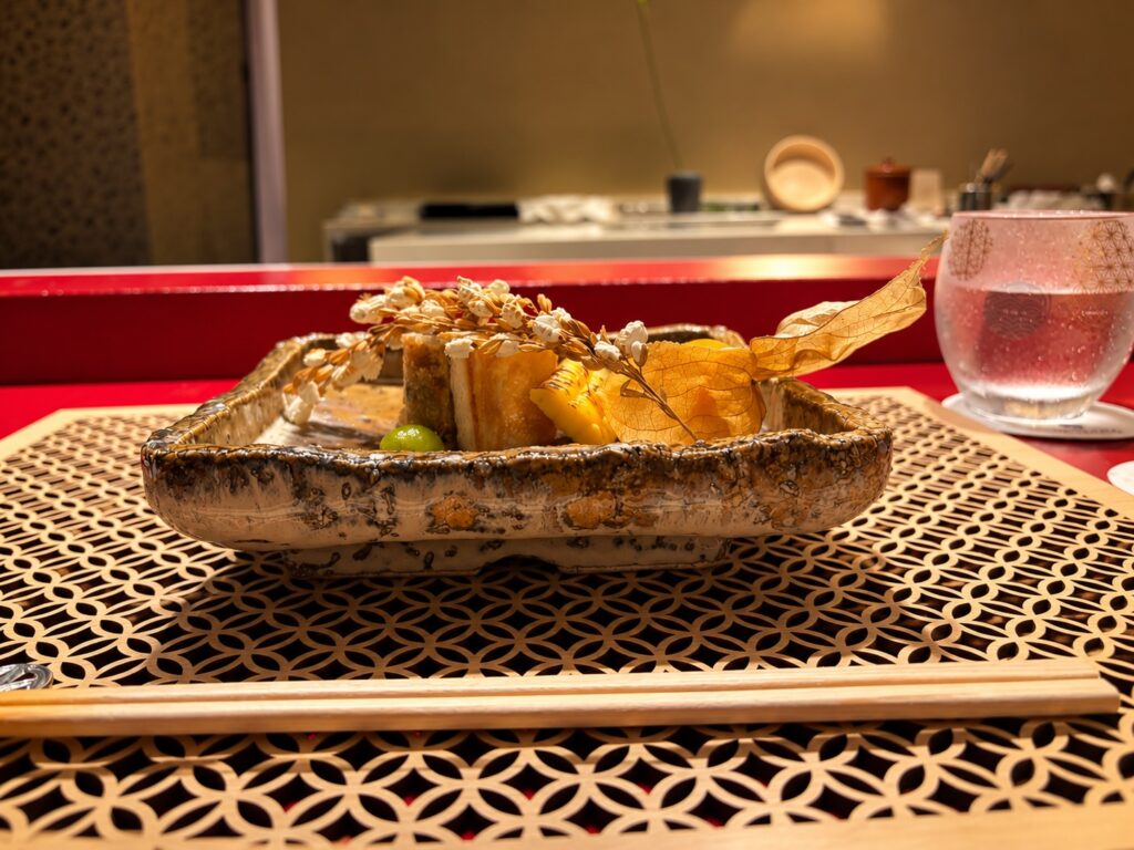 Artfully presented Japanese dish in a dark ceramic bowl on a restaurant table at THE PASONA Natureverse Retreat on Awaji Island, Japan.