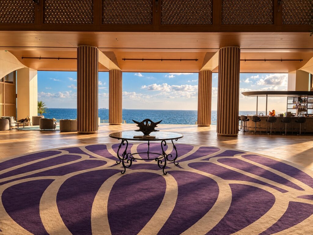 Grand oceanfront lobby at THE PASONA natureverse retreat on Awaji Island, Japan, featuring a purple patterned floor, wooden columns and panoramic sea views.